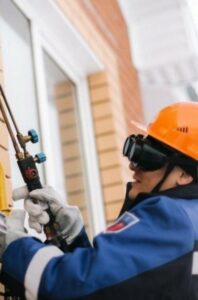 alt="Специалист ogs55.ru проводит пусконаладочные работы газового оборудования на фасаде частного дома"